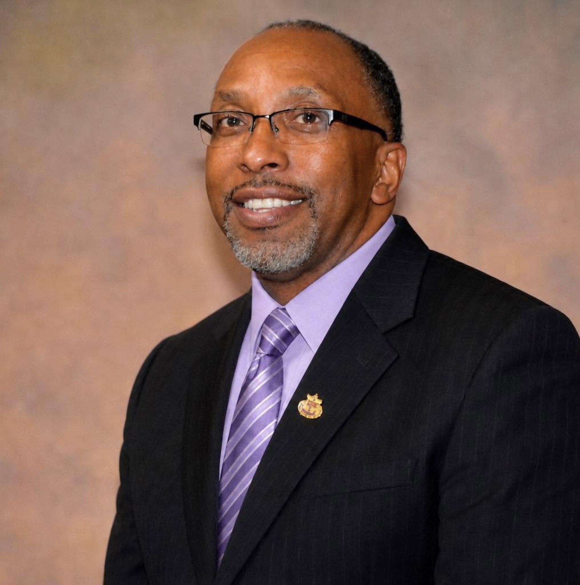 Portrait of Bishop Derrick Fitzpatrick wearing glasses, a dark suit, and a purple tie.
